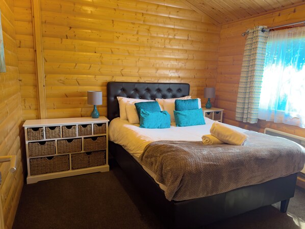 A wooden cabin bedroom with a bed, nightstands, wicker baskets, and a window with curtains.