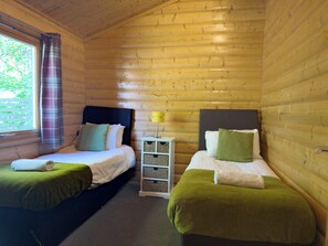 A cabin with two beds, a nightstand, and a window with curtains. - Chestnut Meadow Cabin (East Sussex)