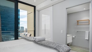 Una habitación de hotel moderna con una cama grande, vista de la ciudad a través de un ventanal y un baño con inodoro y toallero.
