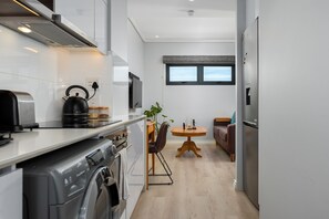 A modern kitchen with a washing machine, a kettle, and a dining area with a table and chairs.