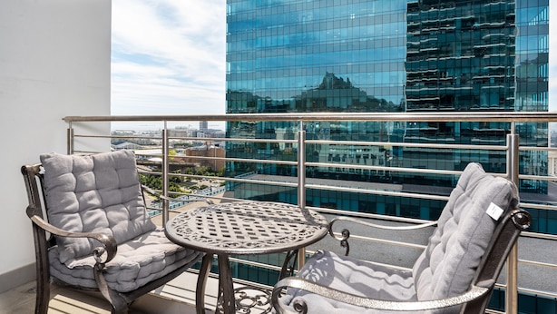 Un balcón con dos sillones acolchados y una pequeña mesa, con vistas a un moderno edificio de cristal.