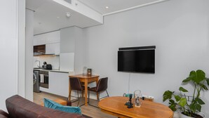 Una sala de estar moderna con un sofá de cuero marrón, una mesa de comedor de madera con sillas, un televisor de pantalla plana montado en la pared y una planta en maceta.