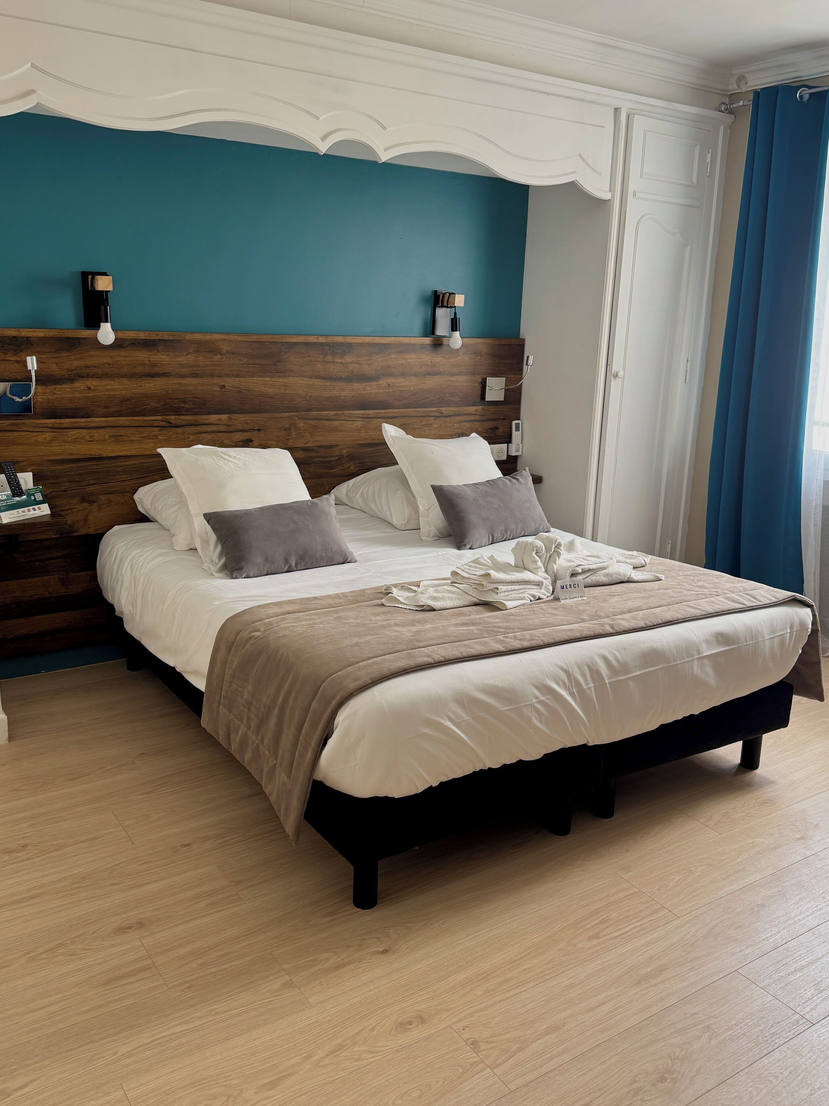 A neatly made bed with a wooden headboard, a bedside table with a lamp, and a blue curtain.