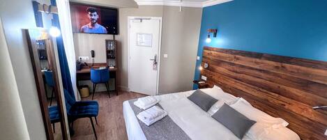 Habitación de hotel con cama, escritorio, silla, televisión y puerta.