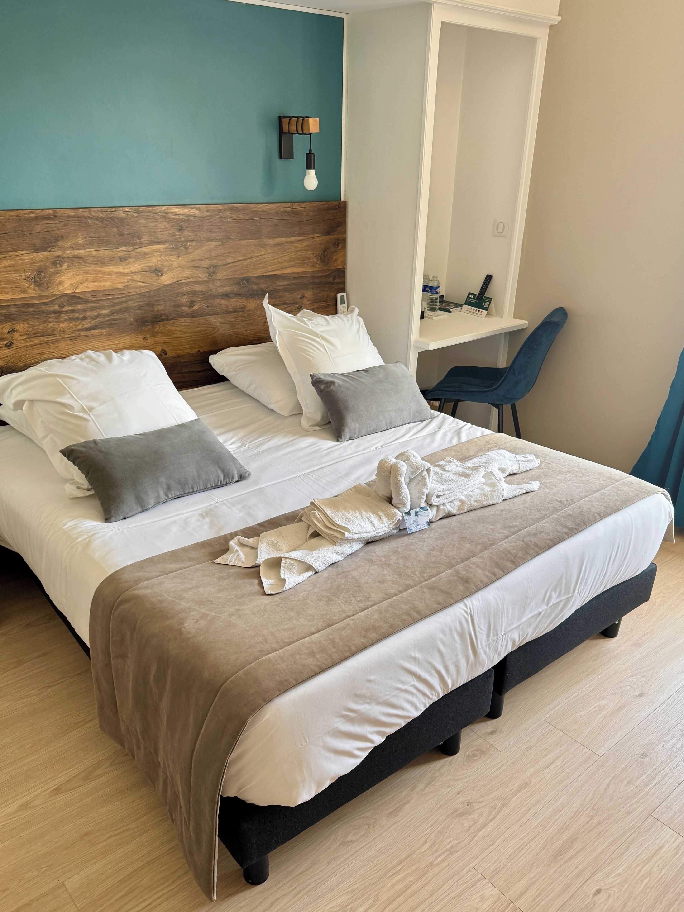 A neatly made bed with white and gray pillows, a beige blanket, and folded towels.