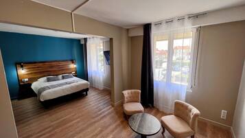 Une chambre d’hôtel avec un lit, une table ronde, deux chaises, un téléviseur et une fenêtre avec des rideaux.