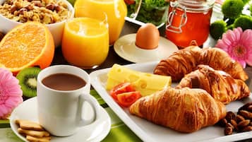 A breakfast setting with croissants, cheese, tomatoes, a cup of coffee, orange juice, and a bowl of granola.