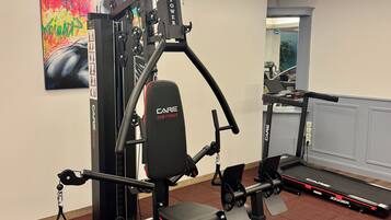 Un gimnasio con cinta de correr, banco de pesas y varias máquinas de ejercicio.