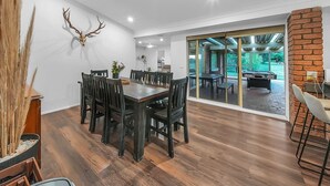 A dining area with a wooden table and chairs, a mounted deer head on the wall, and a view of an outdoor patio with a pool table. - Private House - Pool, Games and Fire Pit Bathurst (Robin Hill)