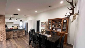 A dining area with a wooden table and chairs, a brick accent wall, and a deer skull mounted on the wall. - Private House - Pool, Games and Fire Pit Bathurst (Robin Hill)