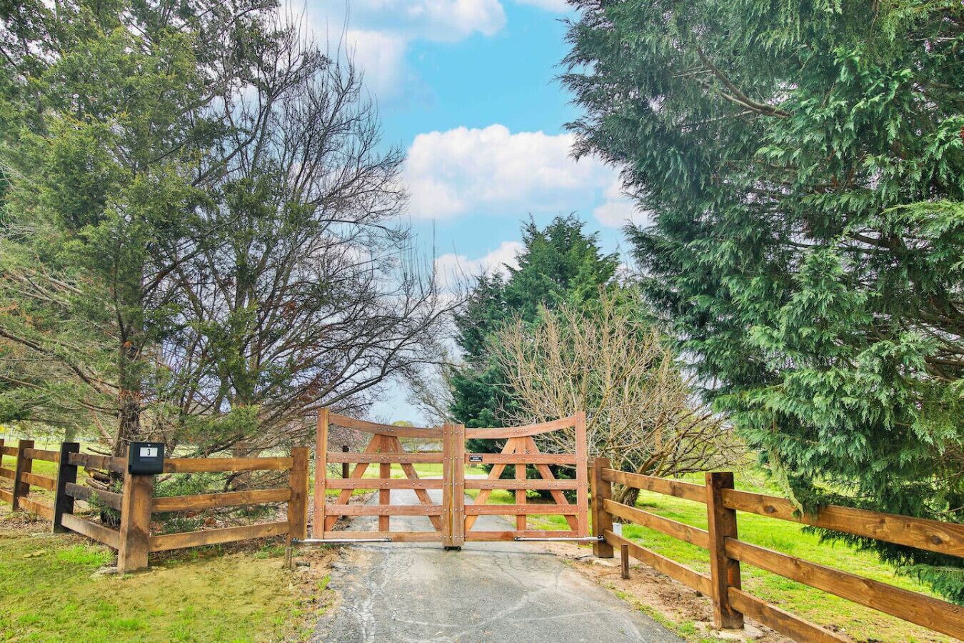 A wooden gate with a metal latch, surrounded by trees and a grassy area.
