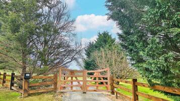 A wooden gate with a metal latch, surrounded by trees and a grassy area.
