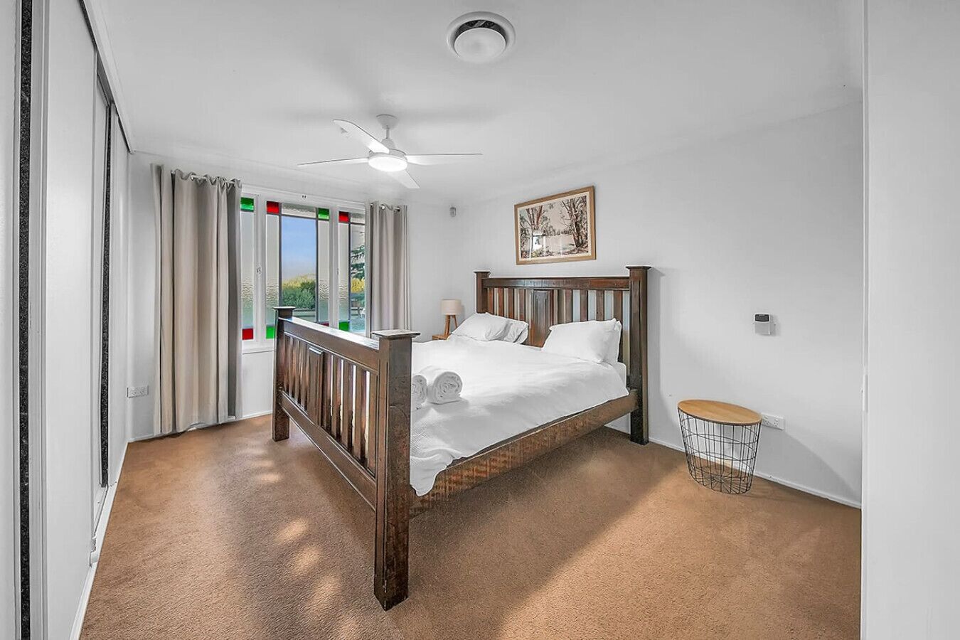 A bedroom with a wooden bed, a ceiling fan, a small round table, and a window with curtains.