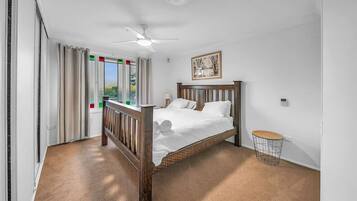 A bedroom with a wooden bed, a ceiling fan, a small round table, and a window with curtains.