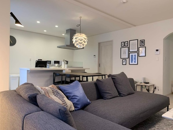 A modern living room with a grey sofa, a dining table, and a kitchen in the background.