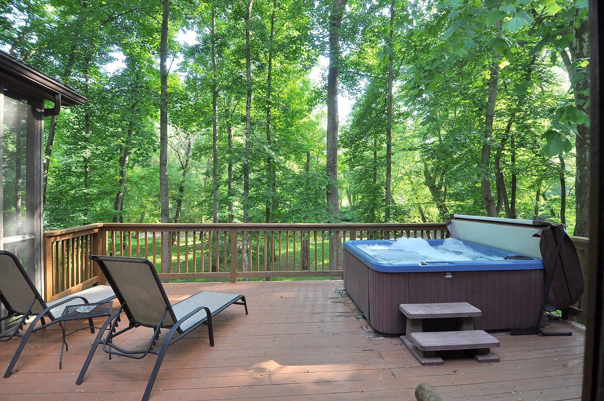 A wooden deck with a hot tub, two lounge chairs, and a picnic table.