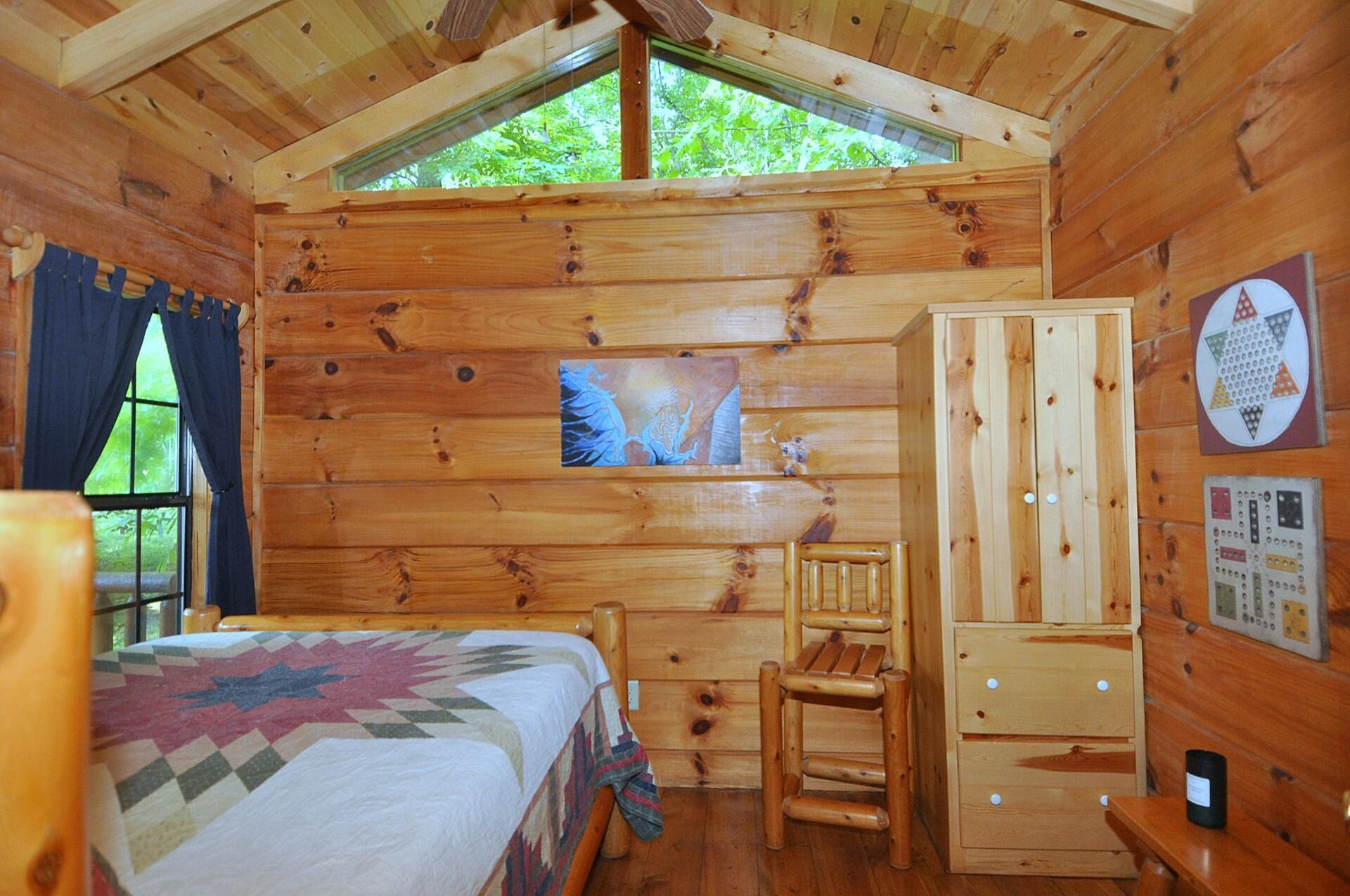 Een gezellig kamer in een blokhut met een bed, een houten stoel, een kast en een raam met uitzicht op begroeiing.