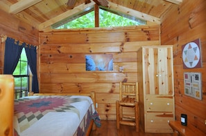 Um quarto de cabana aconchegante com uma cama, uma cadeira de madeira, um armário e uma janela com vista para o verde.