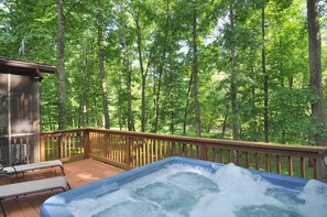 Un jacuzzi en una terraza de madera con vistas a un bosque.