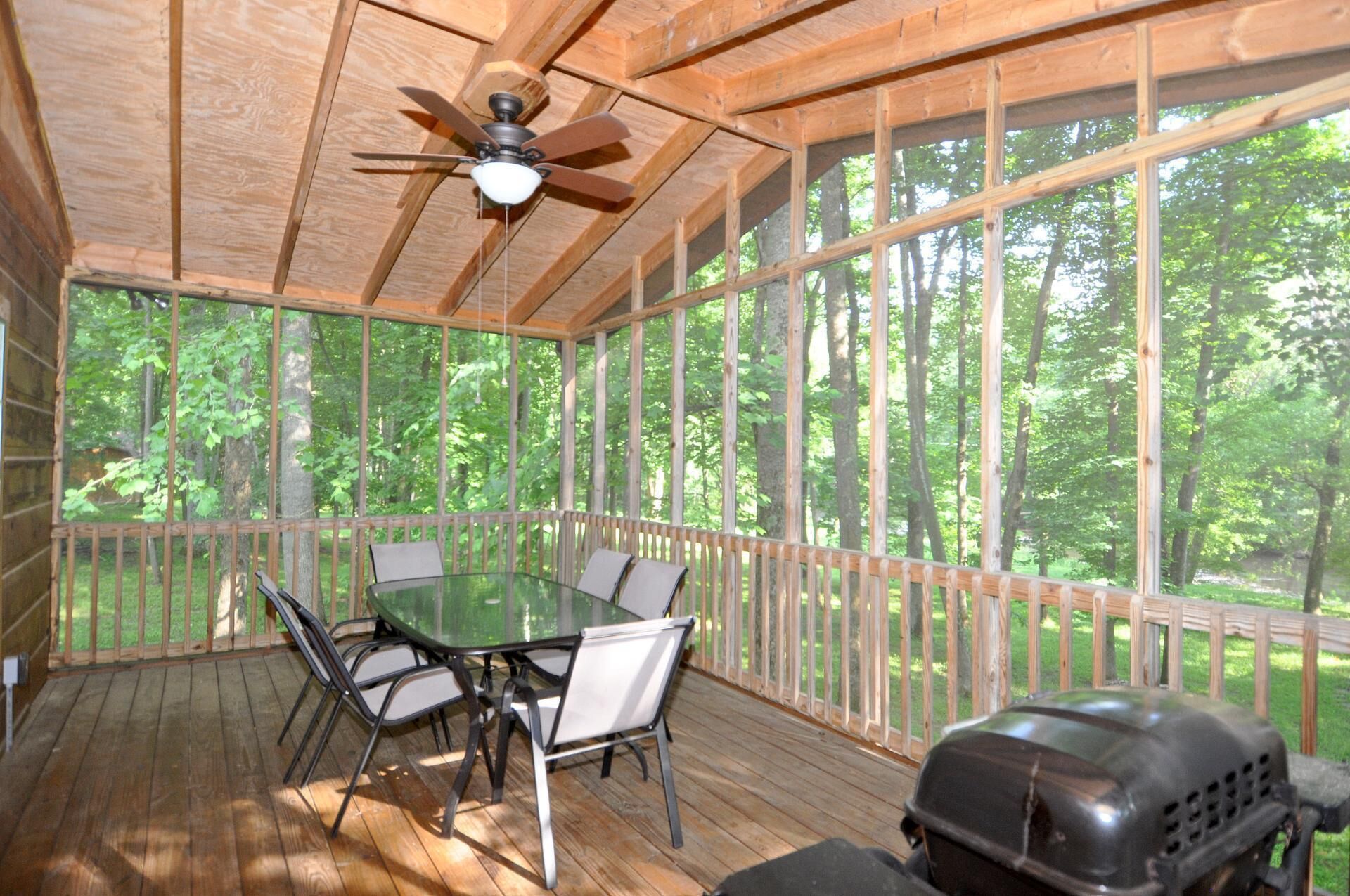 A covered outdoor area with a table and chairs, a ceiling fan, and a grill.
