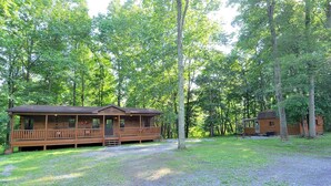 A cabin with a porch and a deck, surrounded by a forest. - Sleepy Creek - Creekside Escape (Berkeley Springs)