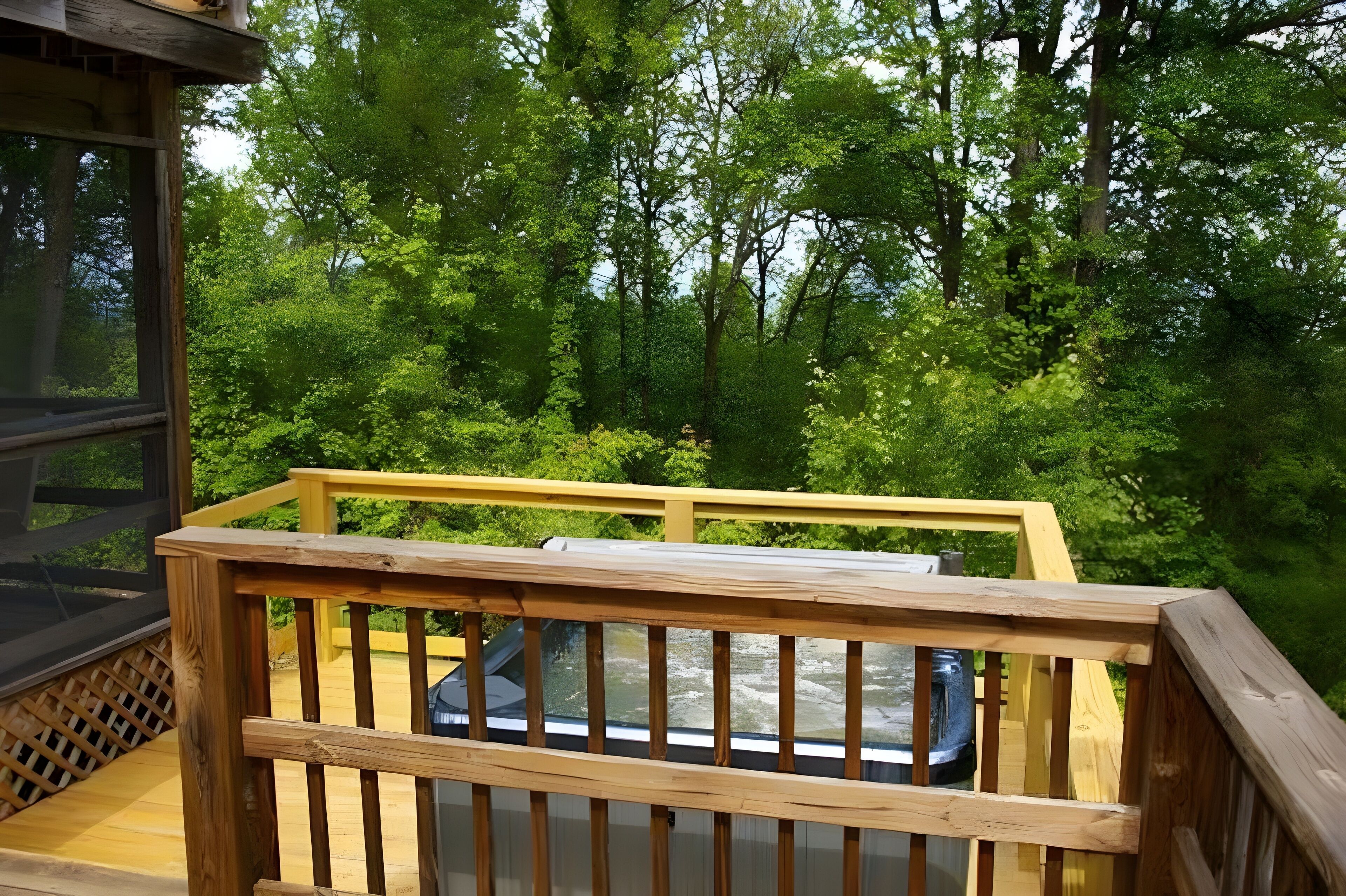 Une terrasse en bois dotée d’une balustrade en verre, qui offre une vue sur une zone boisée.