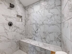 Ein modernes Badezimmer mit Marmorfliesen, einer Duschbrause und einer eingebauten Sitzbank.