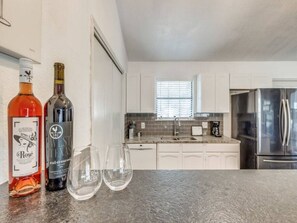 Una cocina moderna con armarios blancos, un refrigerador de acero inoxidable y dos botellas de vino sobre la encimera.