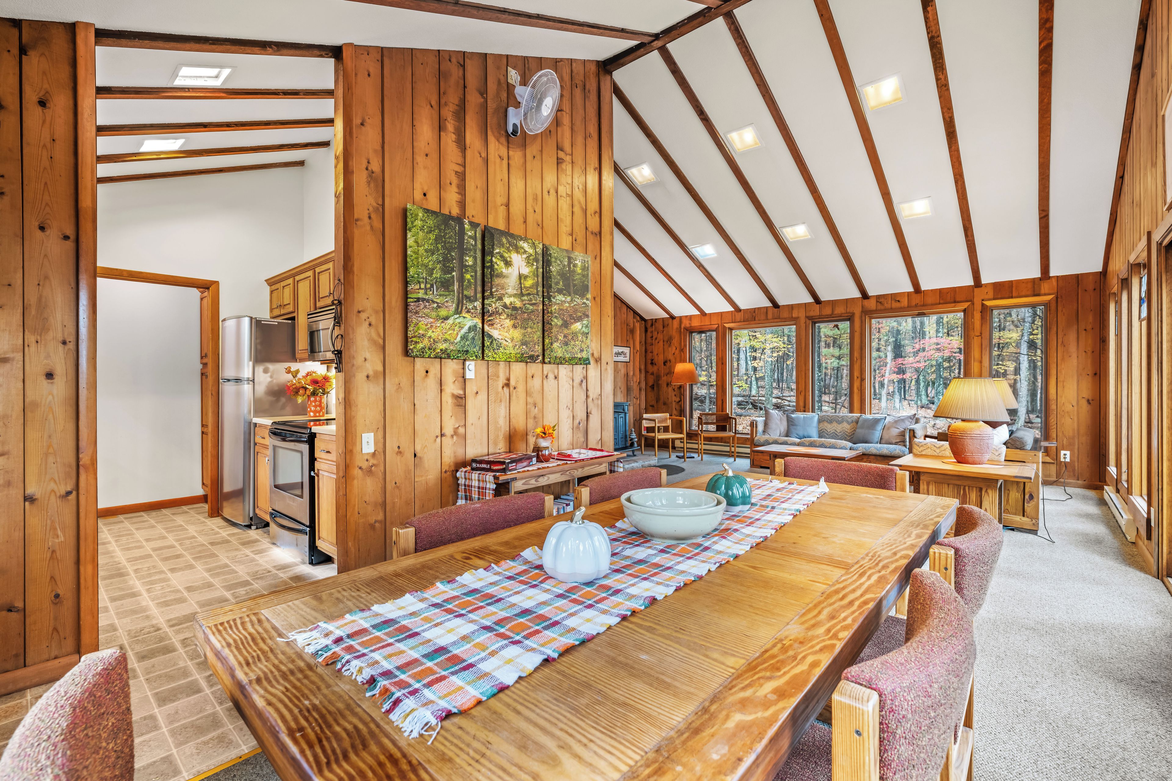 Un intérieur de cabine spacieux comprenant une table à manger en bois, un coin cuisine et un espace salon confortable avec vue sur la forêt.