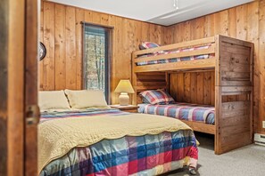 A room with wooden walls, a bunk bed, a single bed, and a window with blinds. - Haven Home (Berkeley Springs)