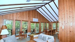 Une cabane en bois dotée d’un grand toit de verre, de meubles en bois et de nombreuses fenêtres offrant une vue sur la forêt environnante.