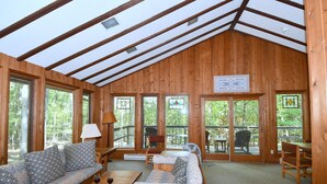 Une cabane en bois avec un plafond haut, de grandes fenêtres et un coin salon confortable avec un canapé et des fauteuils.