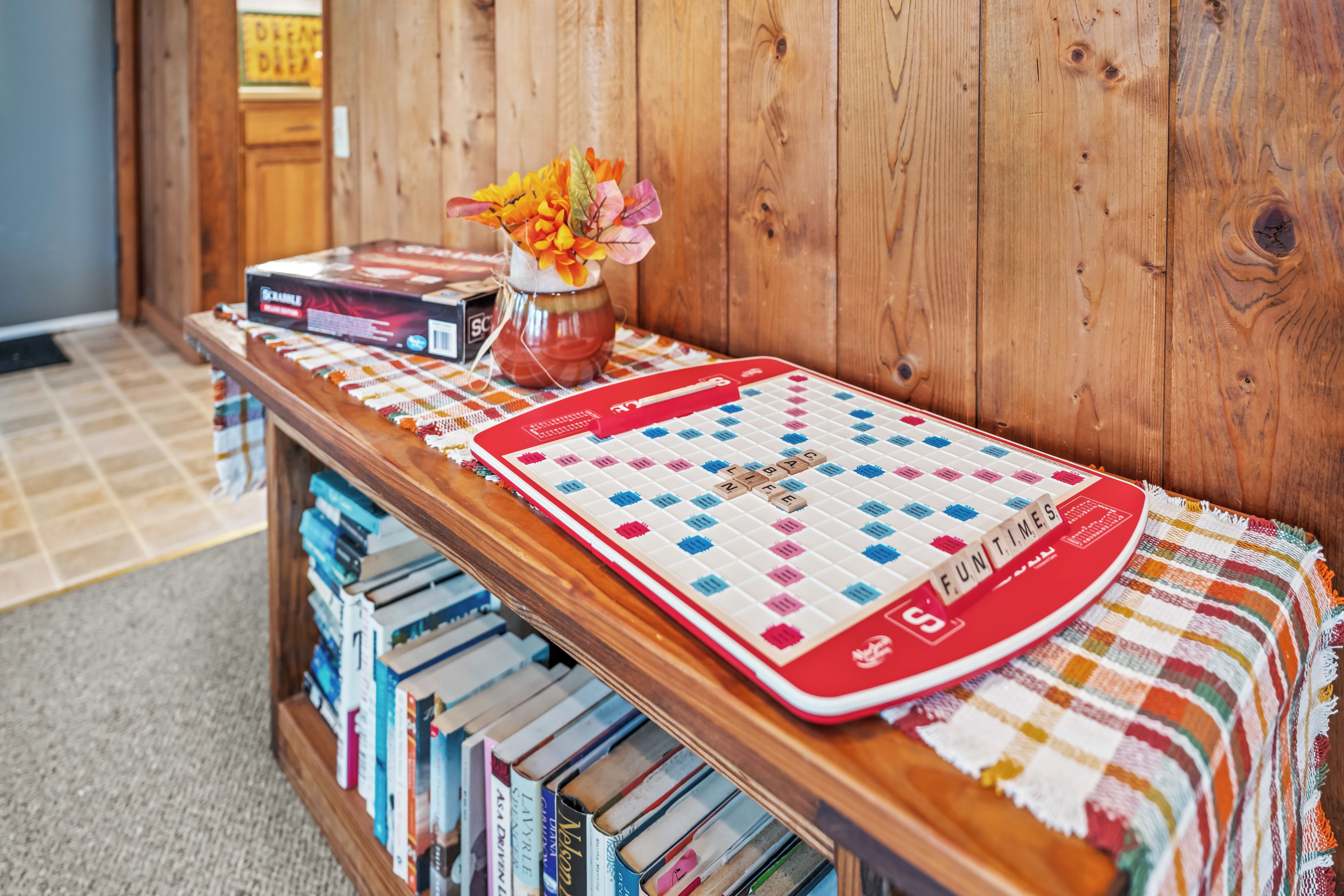 Ein hölzernes Regal mit einem Scrabble-Spiel, Büchern und einer Vase mit Blumen.