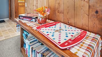 A wooden shelf with a Scrabble board, books, and a vase with flowers.