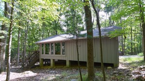 Une petite cabane dotée d’un porche abrité et d’un escalier menant à l’entrée, le tout entouré d’une forêt.