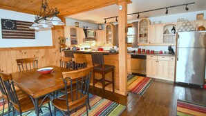 A wooden interior with a dining table, chairs, a kitchen area with cabinets, a refrigerator, and a colorful striped rug. - Seventh Heaven - Heavenly Retreat (Great Cacapon)