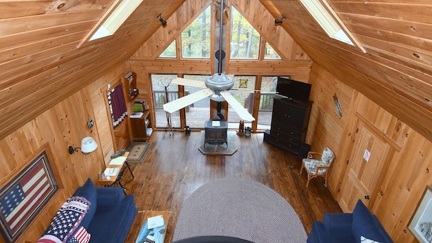 A wooden cabin with a high ceiling, a ceiling fan, a fireplace, and a large window. - Seventh Heaven - Heavenly Retreat (Great Cacapon)