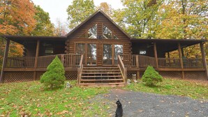 A log cabin with a front porch, a staircase, and a small garden area with a cat. - Seventh Heaven - Heavenly Retreat (Great Cacapon)