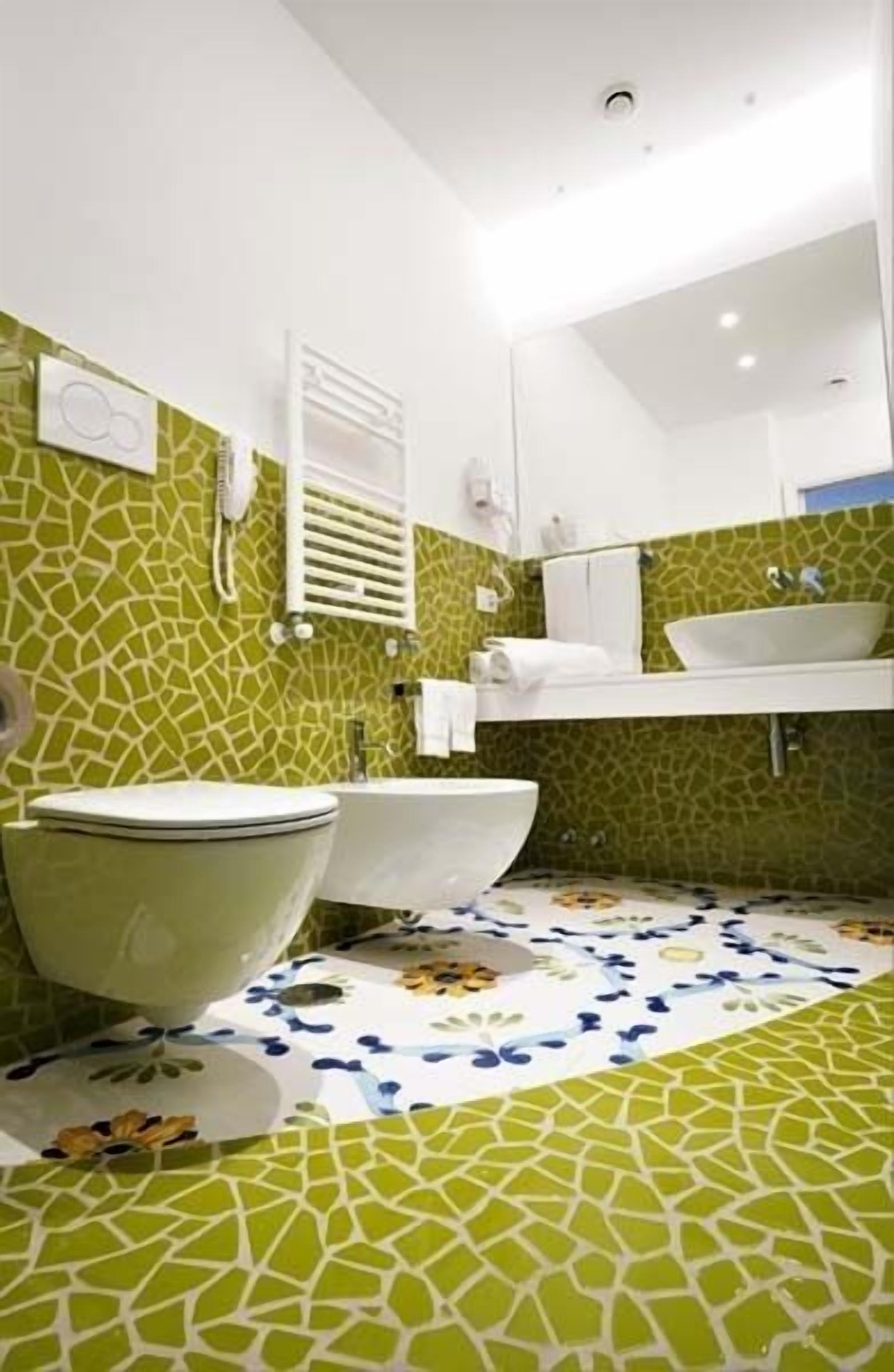 Un baño con pared de mosaicos verdes, un lavamanos blanco, un inodoro blanco y una bañera blanca.