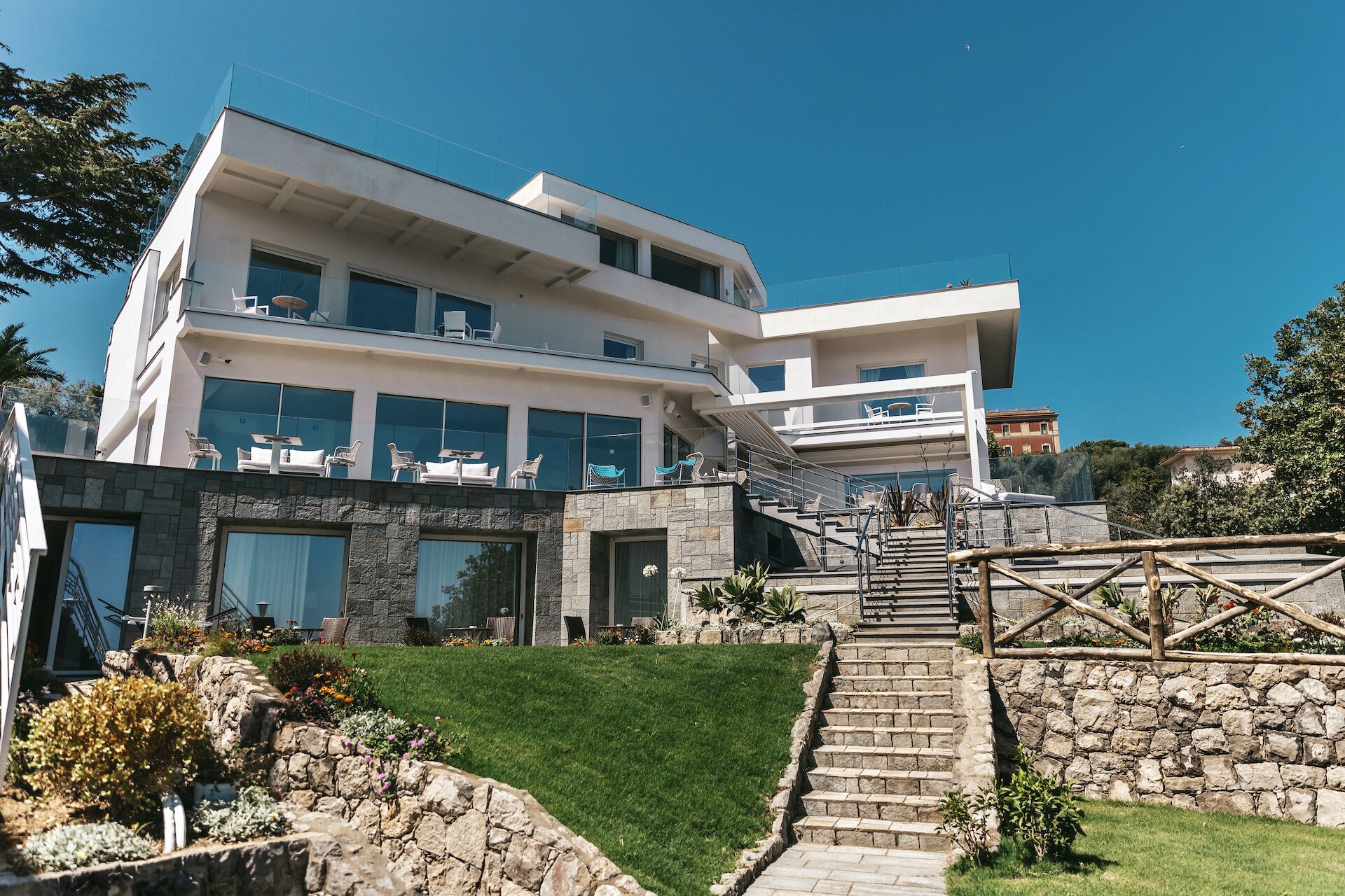 A modern multi-story building with a stone facade, large windows, and outdoor seating areas.