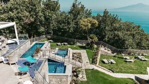 Un área de piscina en la azotea con varias piscinas, sillas de descanso y vistas al mar.