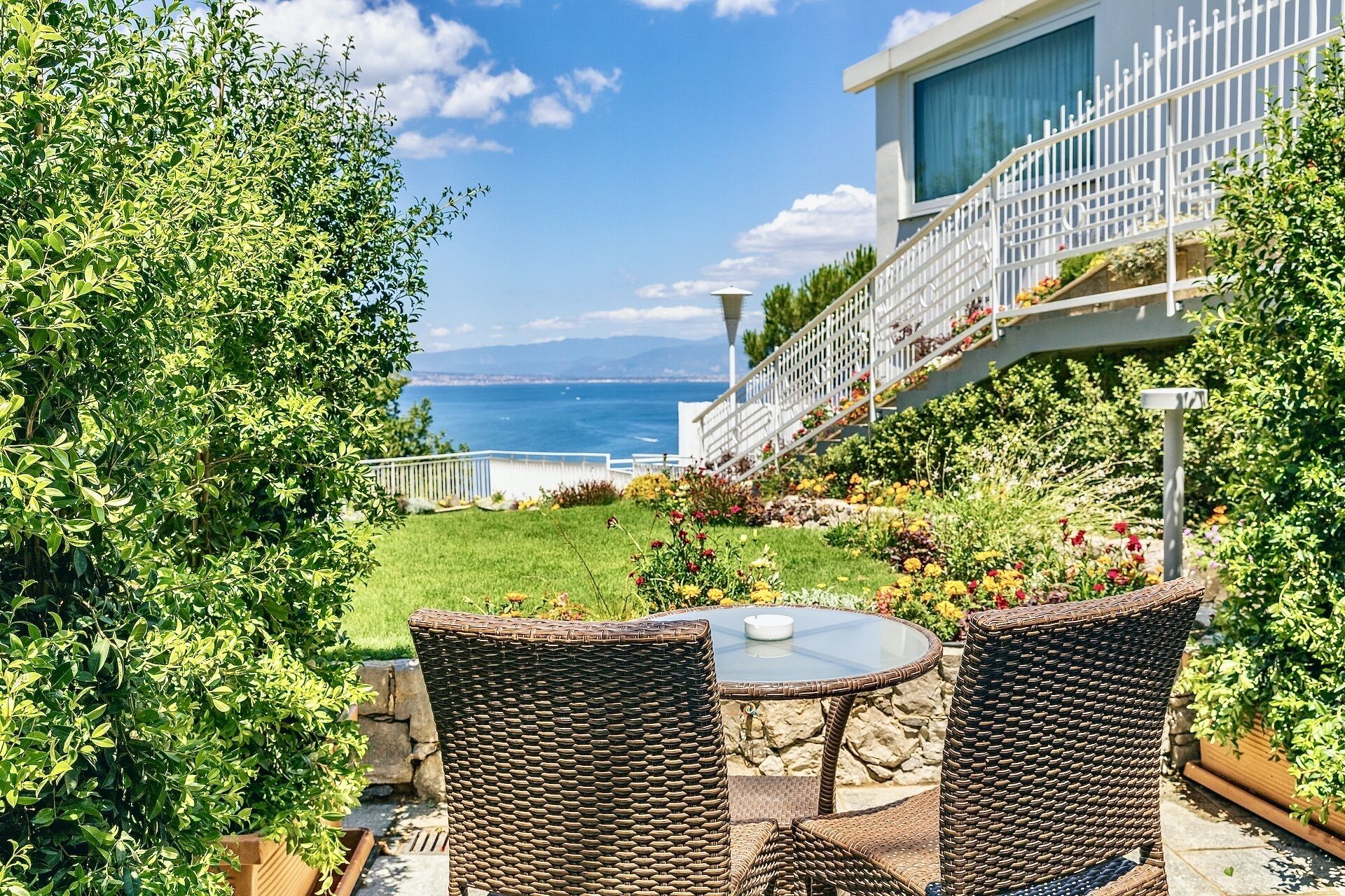 Une terrasse dotée de meubles en osier, d’une table en verre et offrant une vue sur la mer.