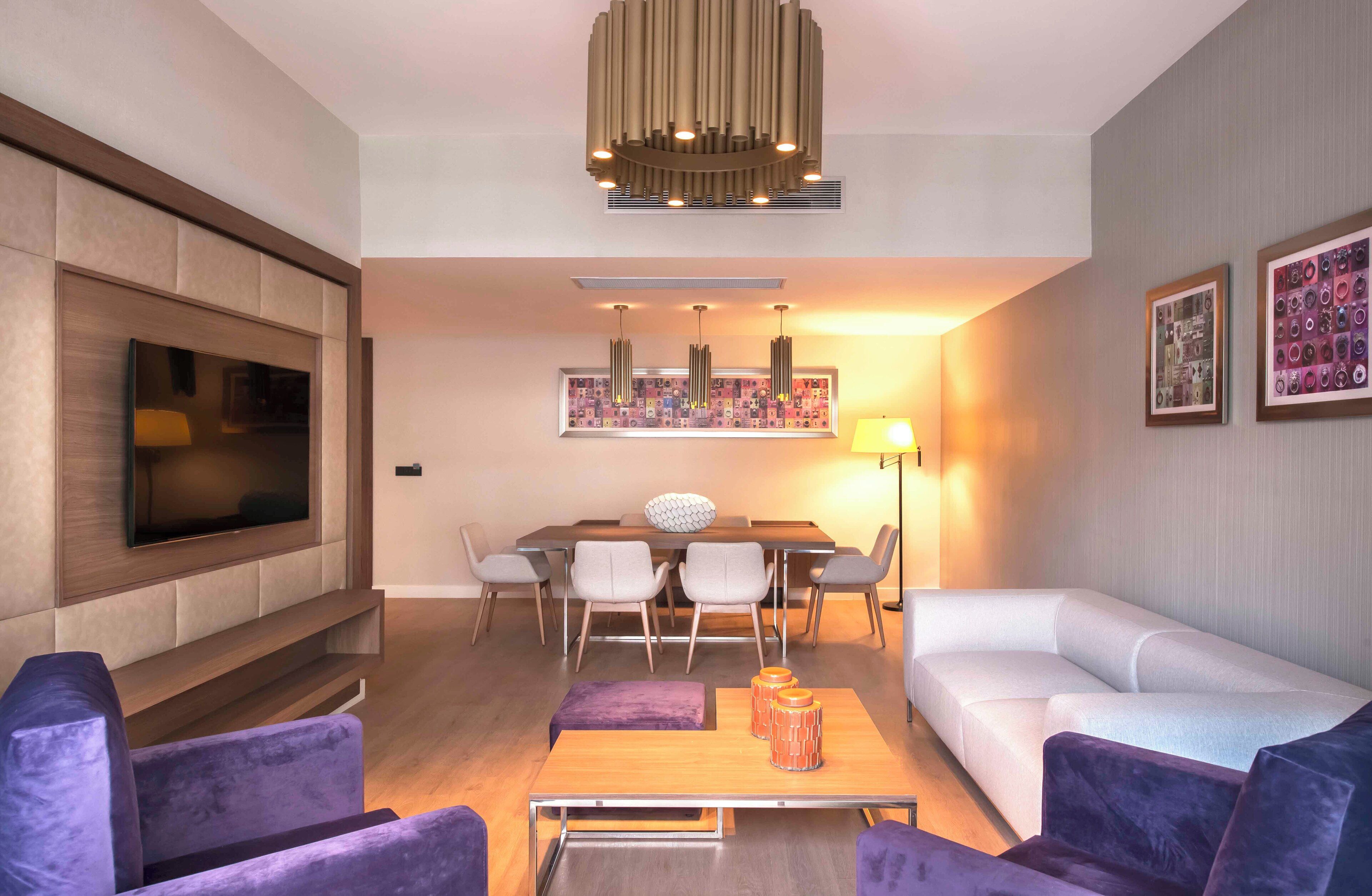 A modern living room with a flat-screen TV, a dining table with chairs, a sofa, and a coffee table.