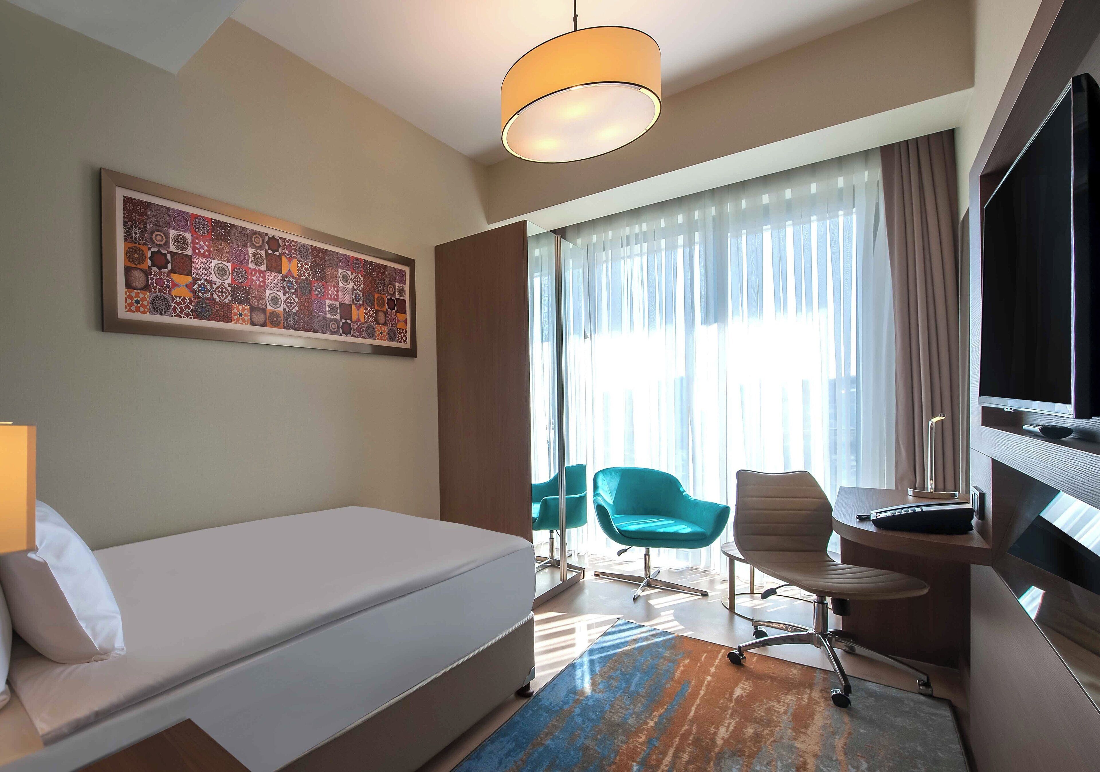 Una habitación de hotel con cama, escritorio, televisor y un ventanal con cortinas.