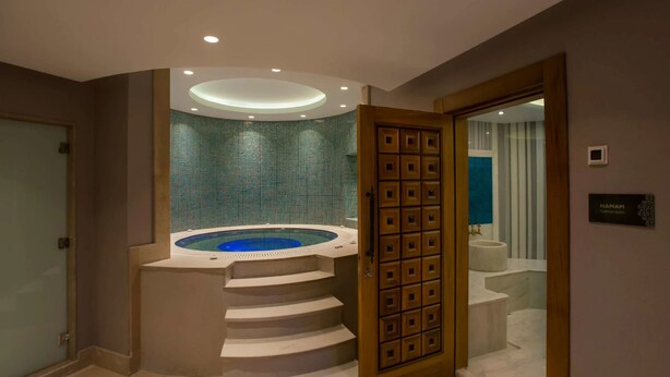 A modern bathroom with a circular hot tub, a wooden door, and a sign reading "HAMAM Turkish Bath". - The Superior Living Batisehir  (Istanbul)