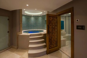 Ett modernt badrum med ett runt bubbelbad, en trädörr och en skylt med texten ”HAMAM – turkiskt bad”.