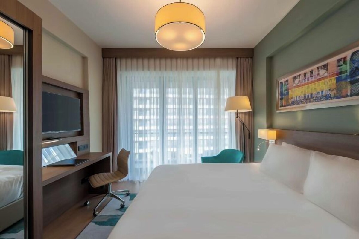 Een hotelkamer met een groot bed, een bureau met computer, een televisie en een raam met gordijnen.