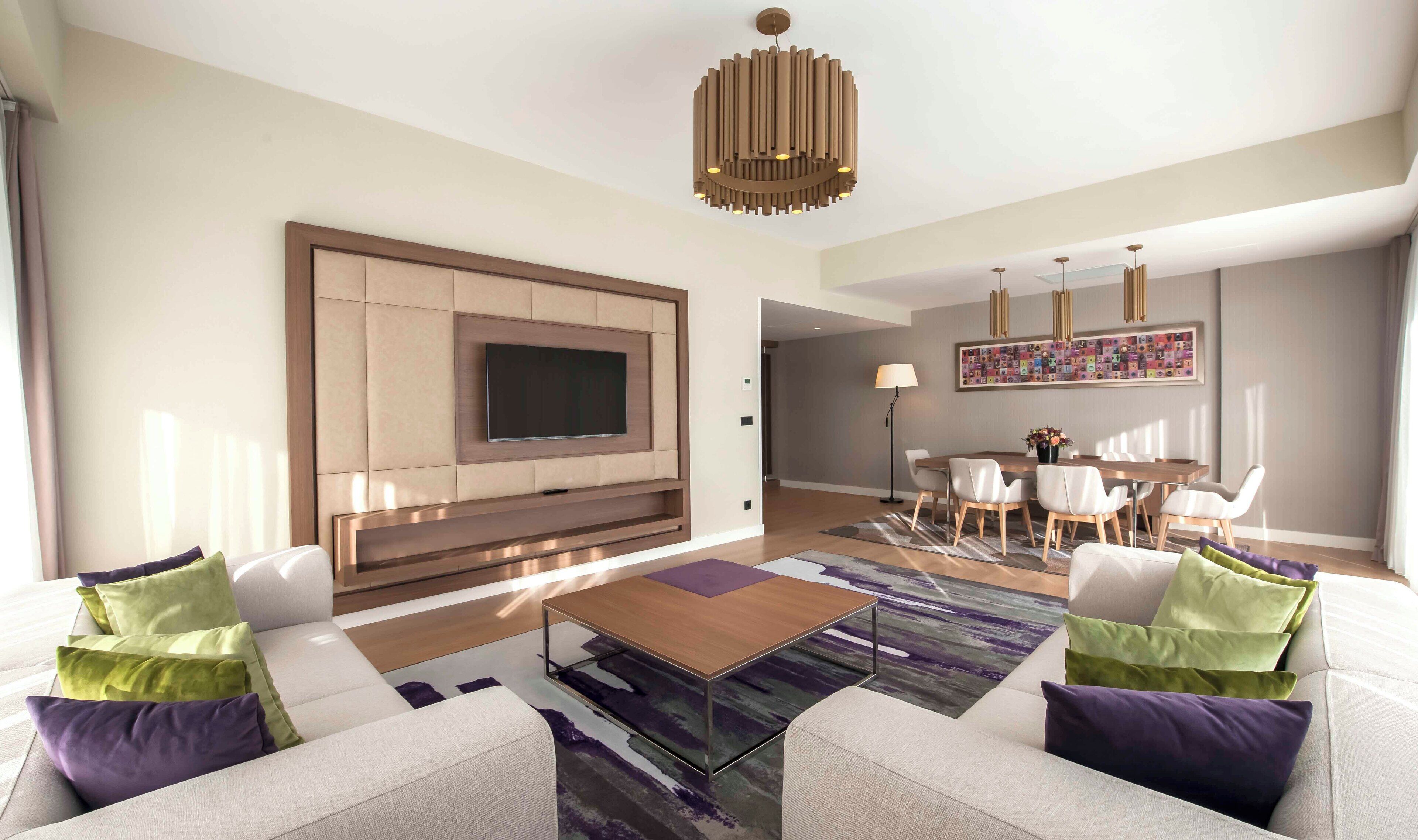 A modern living room with a large flat-screen TV, a sofa set, a coffee table, and a dining area with a table and chairs.