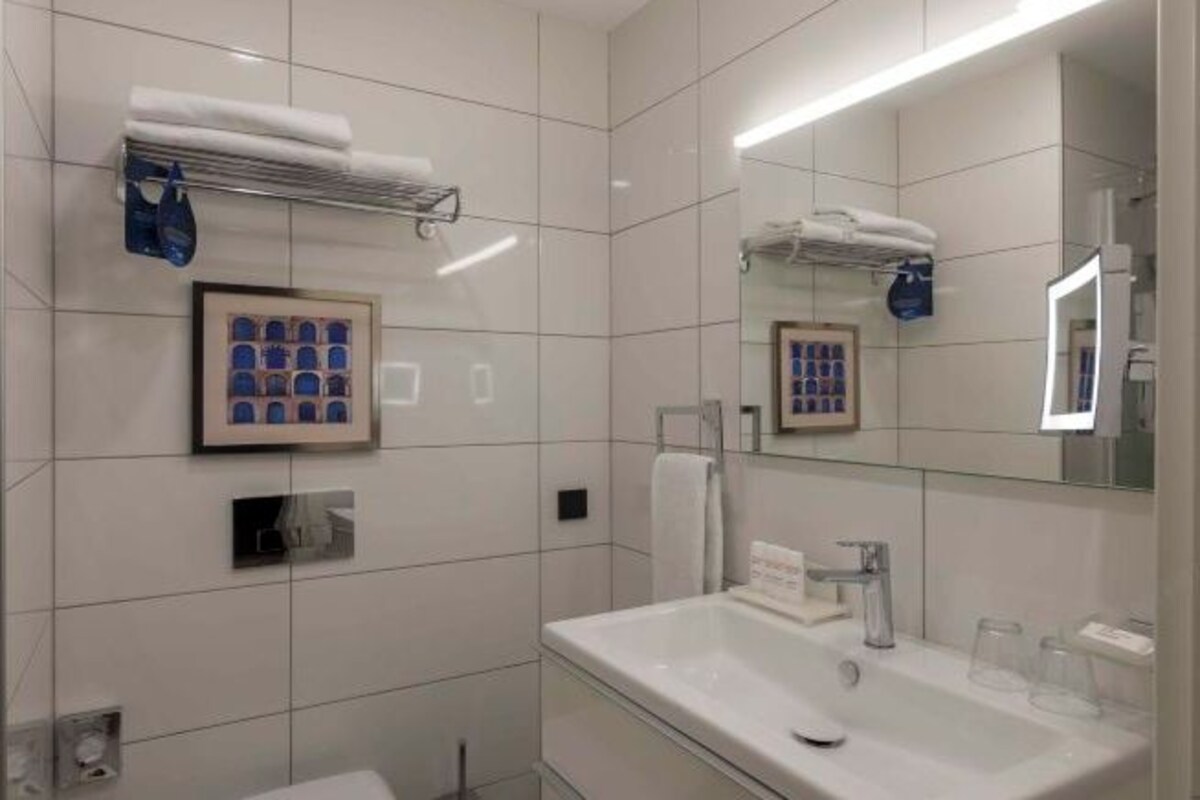A modern bathroom with white tiles, a large mirror, a sink with a faucet, and a towel rack.