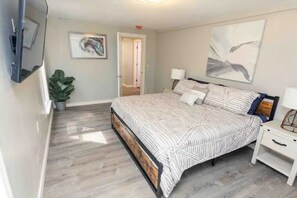 Quarto com cama, mesas de cabeceira, uma planta em vaso e obras de arte nas paredes.